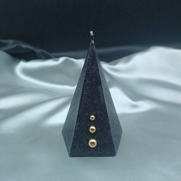 Bougie pyramidale noire Aura Noël avec texture cristallisée et trois perles dorées décoratives sur fond gris satiné.