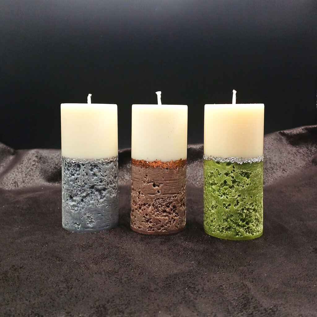 Trio de bougies piliers Alchimie en cire ivoire, avec bases texturées minérales colorées, dans les parfums L’Absolu, Beautiful Day et Boost.